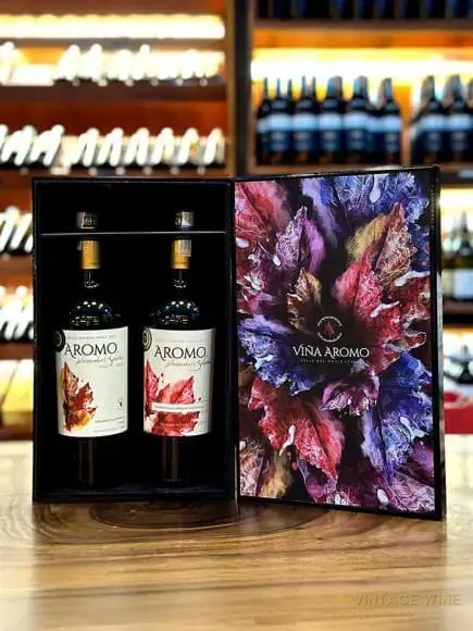 Hộp quà mở nắp đựng hai chai vang Aromo nhãn đỏ, mặt trong nắp in hoạ tiết lá tím đỏ chữ Viña Aromo, đặt trên quầy gỗ